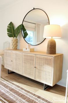 a large round mirror hangs on the wall next to a dresser with a lamp and palm leaf