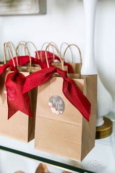 three brown paper bags with red bows on them sitting on a shelf next to donuts