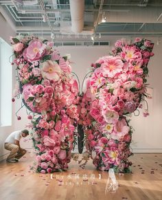 a man kneeling down next to a giant letter made out of pink and white flowers