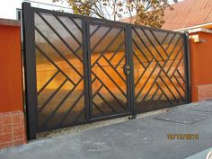 an iron gate in front of a brick building with orange walls and trees behind it