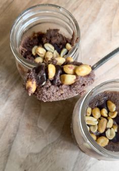 two jars filled with chocolate pudding and nuts on top of a wooden table next to a spoon