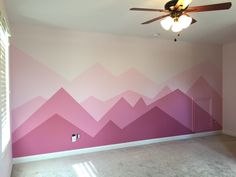 an empty room with pink and white mountains painted on the wall in front of a ceiling fan