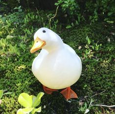 a white duck statue sitting on top of a green grass covered ground next to trees