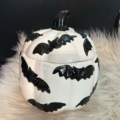 a black and white ceramic pumpkin with bats painted on it's lid sitting on a fur covered surface