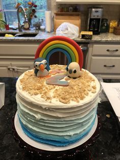 a cake with frosting and two penguins on top sitting on a counter in a kitchen