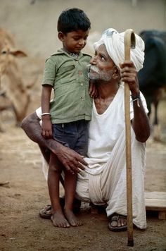 an old man holding a stick with a young boy on his lap next to him