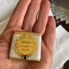 a hand holding a gold and white pin with the word vera alba on it's side