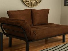 a brown futon couch sitting on top of a wooden floor next to a clock