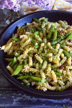 a bowl filled with pasta and asparagus on top of a table next to purple flowers