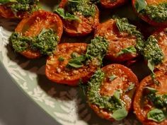 tomatoes with pesto on them sitting on a green and white plate, ready to be eaten