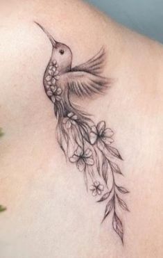 a hummingbird with flowers on its back and wings is shown in this tattoo design