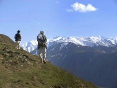 two people walking up a hill with mountains in the background