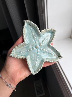 a hand holding a ceramic starfish dish in front of a window