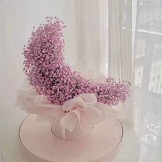 a white hat with pink flowers in it sitting on a table next to a window