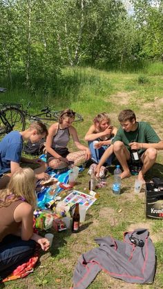 a group of people sitting on top of a grass covered field next to bikes and picnic bags