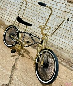 a gold bicycle chained to a brick wall with chains on the front and back wheels