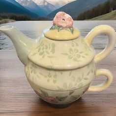 a teapot with a flower on top sitting on a table next to the water