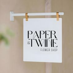 a white paper and twine sign hanging from a clothes line in front of a wall