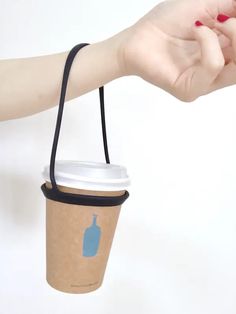 a woman's hand holding a coffee cup with the lid open and a black string attached to it