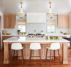 a kitchen island with three stools in it and two lights hanging from the ceiling