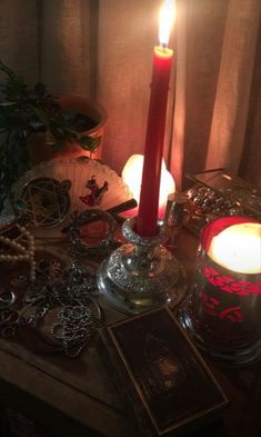 a lit candle sitting on top of a wooden table next to jewelry and a potted plant