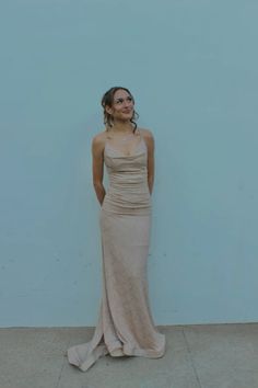 a woman standing in front of a blue wall wearing a long dress and smiling at the camera