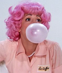 a woman with pink hair blowing a bubble