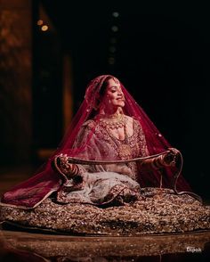 a woman sitting on top of a bed wearing a red veil and dress with gold accents