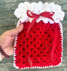 a crocheted red and white bag with a ribbon around the top is held by a woman's hand