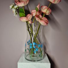 pink and white flowers are in a clear vase on a marble block with purple walls