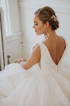 a woman in a white wedding dress sitting on a bed with her back to the camera