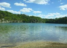 a lake surrounded by trees and rocks under a blue sky with white clouds in the background