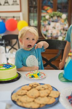 a little boy sitting at a table in front of a cake and cookies on plates