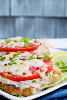 two sandwiches with tomatoes, cheese and lettuce are on a plate next to a lemon wedge