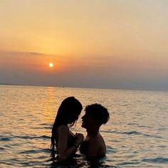 two people in the water at sunset with one holding his arm around the other's neck