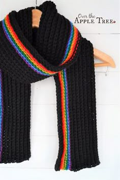 a black scarf with multicolored stripes hanging on a wooden hanger next to a white wall