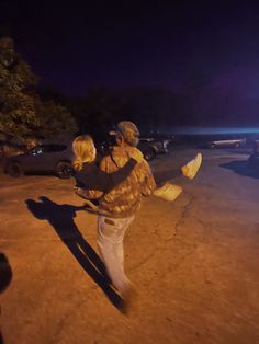 a man and woman walking down the street at night with their arms around each other