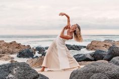 a woman standing on top of a sandy beach next to the ocean with her arms in the air