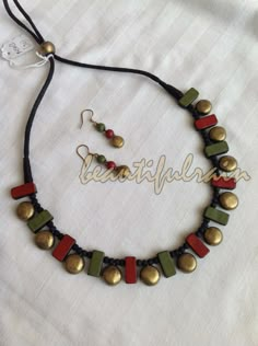 a necklace and earring set on a white cloth with gold, green and red beads