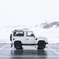 a white jeep parked in a parking lot on a snowy day with mountains in the background