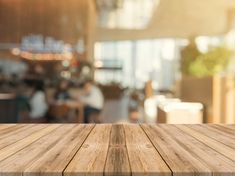 an empty wooden table top in front of a blurry room with people sitting at tables