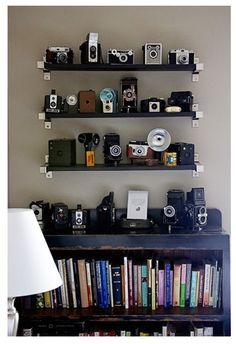 a room filled with lots of books and cameras on top of shelves next to a lamp