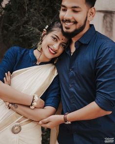 a man and woman standing next to each other in front of a tree smiling at the camera