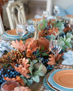 the table is set for thanksgiving dinner with blue and orange plates, silverware, and pumpkins