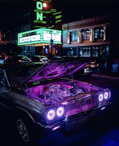 an old car with its hood up on the street in front of a neon sign