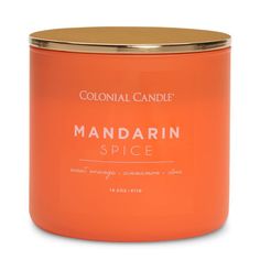 an orange candle with the words mandarin spice in gold rimmed metal lid, on a white background