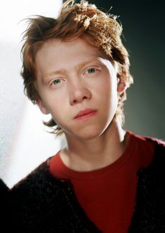 a young man with frizzy hair and blue eyes looks into the camera while wearing a red shirt