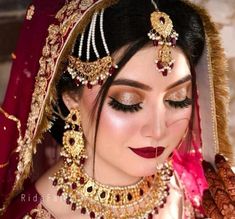 a woman in a red and gold bridal outfit with jewelry on her head, looking at the camera