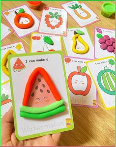 a child's hand is holding up a card with fruit and vegetables on it