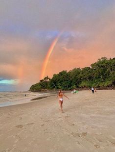 a woman is running on the beach with a rainbow in the sky over her head